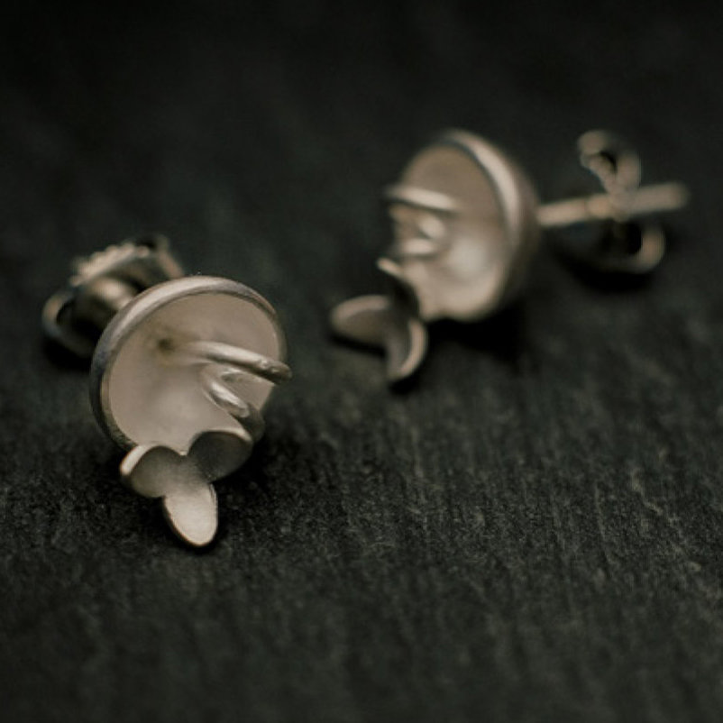 boucles d'oreilles puces en argent composées de petites coques d'où sortent de fines tiges enroulées comme des vrilles et surmontées de petites fleurs à trois pétales.