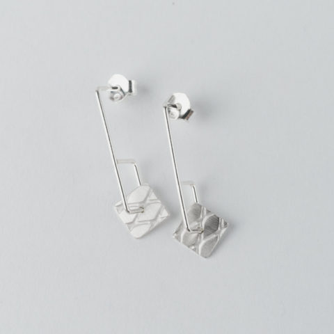 boucles d'oreilles pendantes courtes géométriques en fil d'argent sur lesquelles circulent de petites pastilles carrées avec texture grillage incrustée