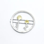 broche ronde en argent et laiton composée de deux fleurs stylisées dans un cercle irrégulier en argent martelé .